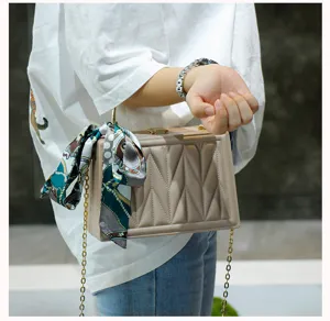 Detailed view of the stylish beige box crossbody bag with silk scarf and gold chain strap.