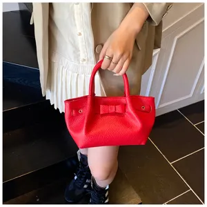 Red leather handbag detailed shot featuring a chic bow and metal grommets, trendy style.