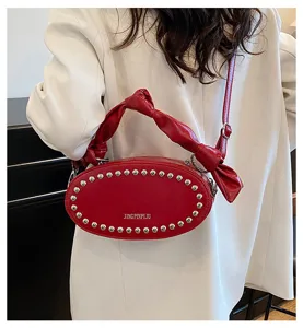 Detail shot of red oval shoulder bag with metal rivets and stylish knotted handle design.