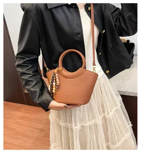 Stylish brown leather vegetable basket shoulder crossbody bag with round handle and bead charm.