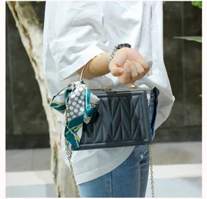 Quilted box handbag with metal handle and elegant silk scarf, stylish cross-body bag.
