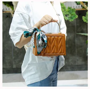 Detailed view of trendy brown box shoulder bag with chic silk scarf and metal handle.