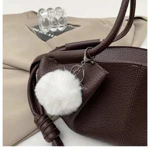 Brown leather dumpling bag with white plush pom pom charm, stylish casual shoulder bag.