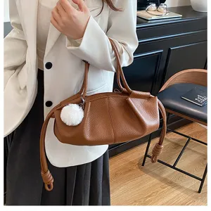 Detail view of the brown leather drawstring dumpling handbag with fluffy pompom charm for women.