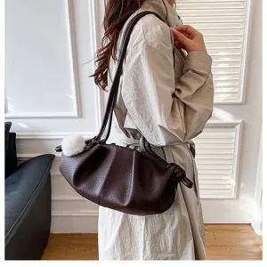 Detail shot of a dark brown leather pleated dumpling cloud shoulder bag with a cute white pompom.