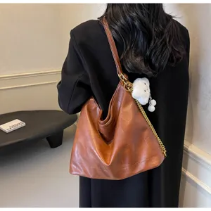 Detail shot of brown leather hobo shoulder bag with cute plush bear pendant, casual daily style.