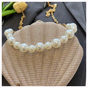 Gold sparkly shell evening bag with pearl handle and chain strap, stylish shoulder bag detail.
