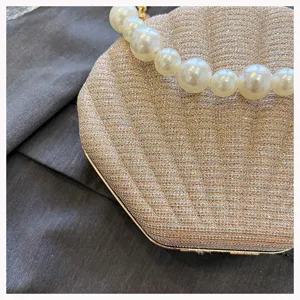 Detail shot of a glamorous gold glitter shell clutch bag with large pearl handle accent.