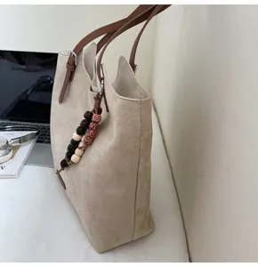 Nahaufnahme einer lässigen, beigen Veloursleder-Tasche mit braunen Trägern und Holzperlen.