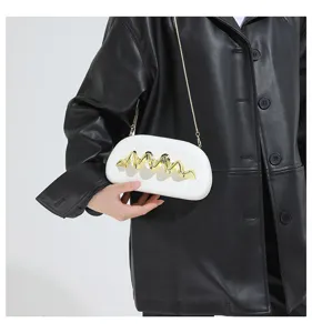 Detailansicht der weißen Clutch mit goldenem Wellen-Dekor und Kette, stilvolles Mode-Accessoire.