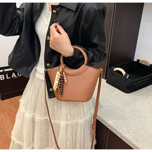 Detailed view of brown leather bucket bag with top handle and charming beaded pendant decoration.