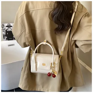 Détail de petit sac à main en cuir verni blanc avec charmant pendentif cerise.