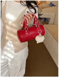 Detailed shot of a stylish red cylinder boston bag with cute plush sheep pendant, chic.