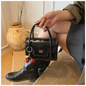 Vue détaillée d'un élégant sac à main noir en cuir verni avec charmant pendentif cerise.