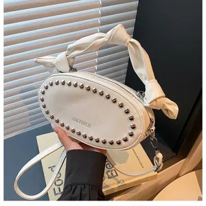 White leather handbag with metal rivets and knotted handle, stylish shoulder bag detail.