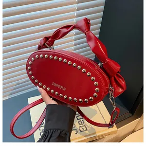 Red oval studded shoulder bag with knotted handle, stylish PU leather crossbody bag detail.