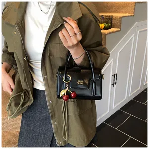 Vue détaillée d'un élégant sac à main noir en cuir vernis avec un charmant pendentif cerise.