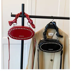 Stylish oval rivet crossbody bag with shiny oil leather finish and elegant handle bow detail.