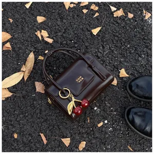 Petit sac à main marron foncé de style vintage avec charm cerise et détail de lettres dorées.