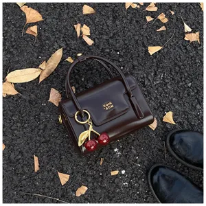 Vue détaillée d'un mini sac à main rétro marron foncé avec pendentif cerise sur l'asphalte.