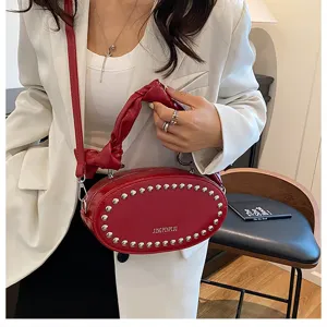 Detail shot of a red leather crossbody bag with metal studs and knotted handle in a chic setting.