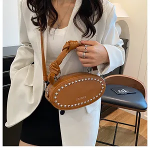 Detailed view of the brown oil leather oval crossbody bag with metal rivets and knotted handle.
