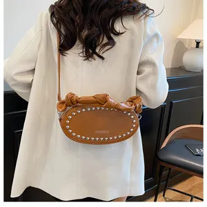 Brown oval leather shoulder bag detail showing metal studs and unique knotted strap design.