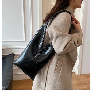 Retro black glossy shoulder bag for women, stylish underarm tote with metal grommet details.