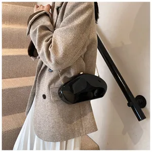 Close-up view of black irregular acrylic evening clutch bag with metal chain on model.