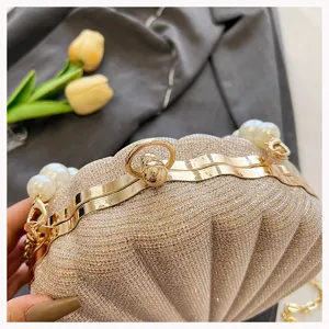 Detailed shot of glittering shell-shaped evening bag with pearl decor and gold metal clasp.