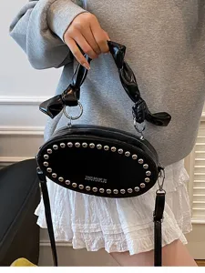 Black oval leather crossbody bag with metal rivets, stylish knotted handle and shoulder strap.