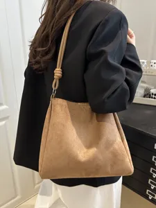 Detailed view of brown suede shoulder bag with stylish knotted handle worn by model indoors.