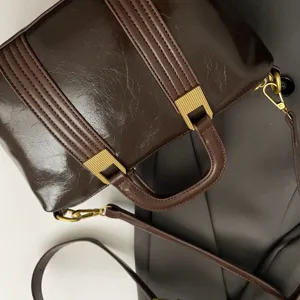 Detailed view of the dark brown glossy leather handbag featuring stylish metallic gold hardware.