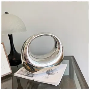 Vista detallada de un elegante bolso de mano de metal plateado, diseño escultórico moderno.