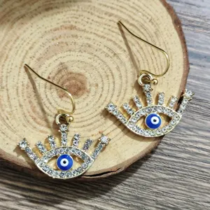 Detail view of stylish gold-toned evil eye earrings featuring sparkling rhinestones and blue enamel.