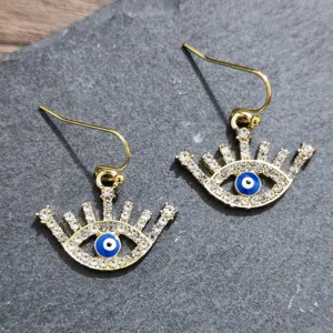 Close-up detail of rhinestone evil eye hook earrings with blue enamel accent on slate.