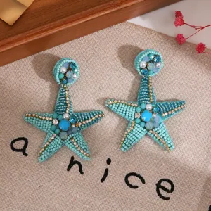 Gros plan des boucles d'oreilles étoile de mer perlées à la main, strass brillants, plage.