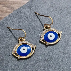 Detail shot of golden rhinestone evil eye earrings featuring blue enamel and sparkling crystal stones.