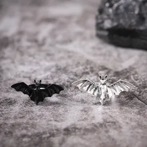 Detailed close-up shot of gothic bat rings in black and silver finishes on textured stone.