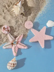 Orecchini a stella marina perlinati rosa primo piano strass brillanti su sfondo di sabbia
