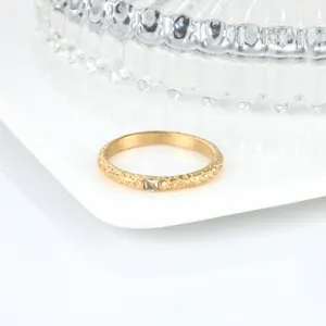 Détail d'une bague en acier titane doré avec surface texturée et pierre carrée.