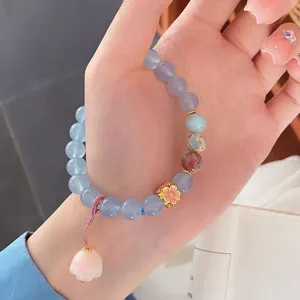 Close-up detail view of blue natural stone beaded bracelet with pink flower on hand.