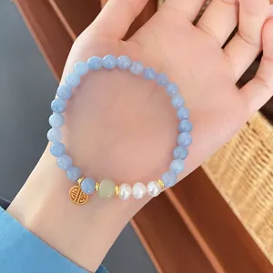 Close-up detail of light blue natural stone and pearl bracelet with gold pendant and jade bead.