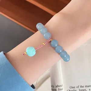 Close-up of light blue natural stone bracelet with delicate flower pendant and pink woven cord.