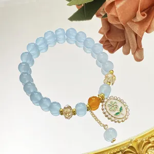 Charmant bracelet de perles de cristal bleu clair avec pendentif fleur et touches dorées.