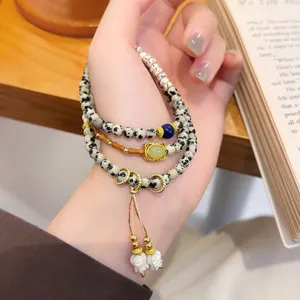 Nahaufnahme des mehrlagigen Perlenarmbands mit Retro-Quaste und Steindetails an Hand.
