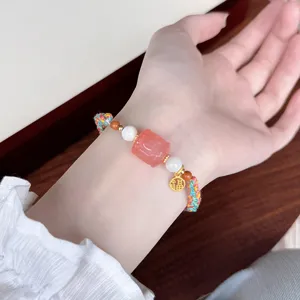 Detailed close-up of an ethnic braided bracelet featuring a pink carved bead and lucky charm.