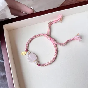 Close-up detail of the pink braided charm bracelet featuring a crystal pixiu and pearl accent.
