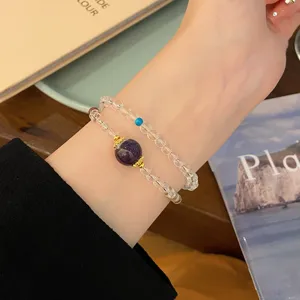 Gros plan détaillé d'un bracelet en cristal blanc double brin avec perle violette dorée.