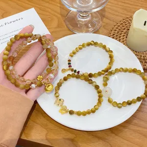 Detail view of multi-layered yellow crystal and tiger's eye bead bracelets with cute gold charms.